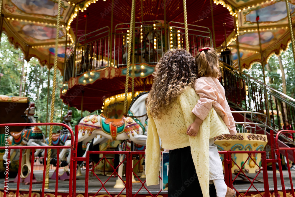 Fototapeta premium Joyful moments shared between a mother and daughter at an enchanting amusement park carousel