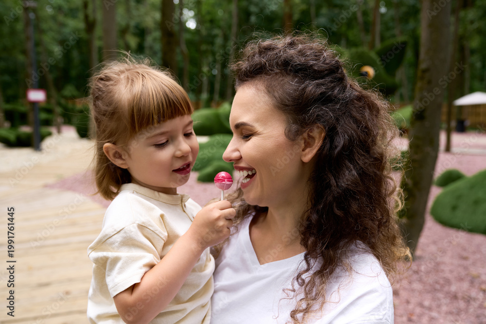 Fototapeta premium Joyful moments between a mother and daughter in a vibrant amusement park setting