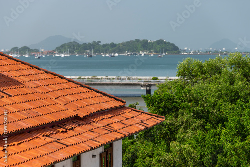Warm terracotta roof tiles contrasting against the deep blue ocean with numerous boats anchored in the bay, creating a scenic view of Panama city's historic district - stock photo