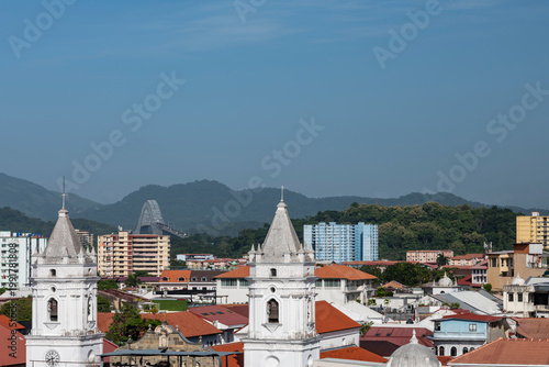 Casco viejo historic quarter of Panama city showcasing colonial bell towers and tiled rooftops with the modern Bridge of the Americas spanning the skyline under a blue sky - stock photo