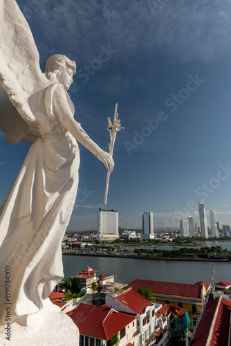 Angel statue standing guard over the historic Casco viejo district with modern skyscrapers and Panama bay forming a vibrant blend of old and new urban landscape - stock photo
