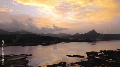 Moving drone shot of Sunset over a lake with dramatic clouds and Mountains in the background shot during monsoon. 4K60fps