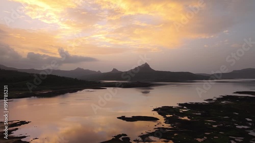 Moving drone shot of Sunset over a lake with dramatic clouds and Mountains in the background shot during monsoon. 4K60fps