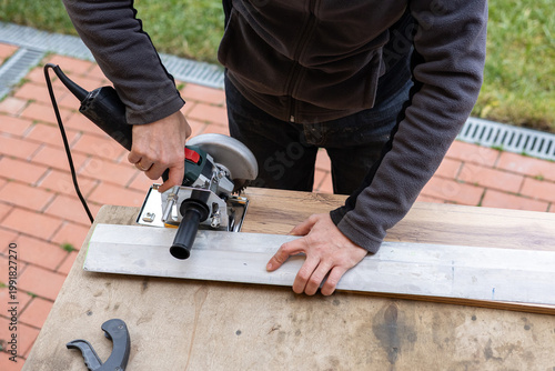 Man cutting a metal channel with a circular saw on an outdoor workbench, DIY home renovation, power tool construction work.