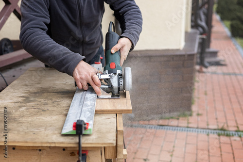 Man cutting a metal profile with a circular saw on an outdoor workbench, DIY home renovation project, construction tools in use.
