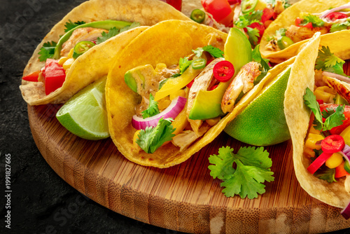 Mexican tacos with pulled chicken, avocado, chili peppers, limes and cilantro, a close-up on a black background