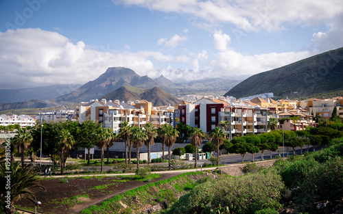 View of Los Cristianos, a popular coastal town in Tenerife, Canary Islands. The image shows a vibrant seaside city with beaches, harbor, and surrounding mountains along the Atlantic Ocean. This scenic