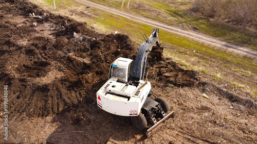 drone photograph of a white wheeled excavator in the process of clearing and leveling earth.