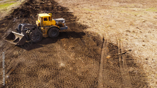 A high-angle aerial photograph of a classic yellow heavy-duty tractor equipped with a front loader bucket is Clearing Dirt at Construction Site