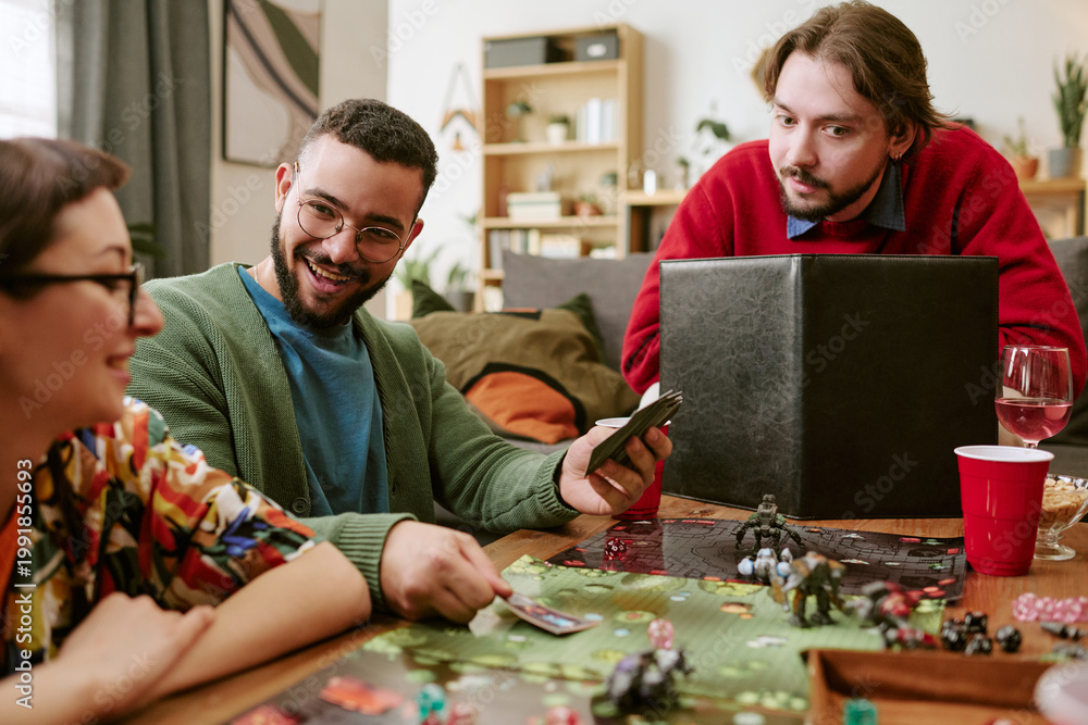 Fototapeta premium Young adult friends playing tabletop role playing game, holding cards and planning moves at home