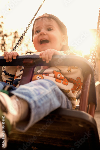 Happy toddler on playground swing at sunset.