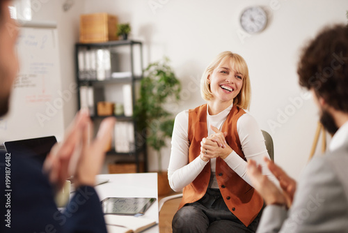 A business team gathers in an office space for a brainstorming session during the morning. A member smiles and claps in response to an idea shared by a colleague, showing the spirit of teamwork.