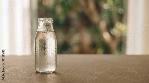A cold glass bottle of water sits on a table indoors.