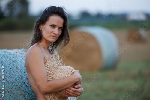 Young woman in countryside holding straw hat, natural summer portrait with hay bales