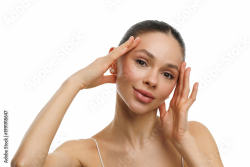 Close-up shot of young white-skinned woman gently touches her face on white background