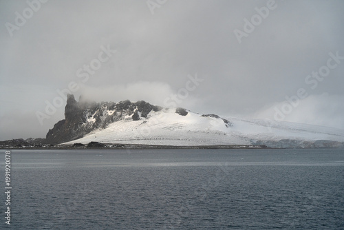 Antarctic expedition. View of snow-covered mountain and calm water under cloudy sky in a remote location during an overcast day. Antarctic Peninsula