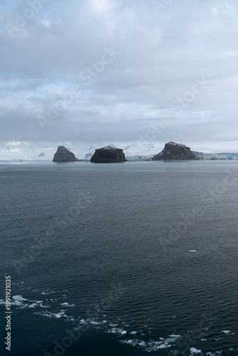 Antarctic expedition. View of snow-covered mountain and calm water under cloudy sky in a remote location during an overcast day. Antarctic Peninsula