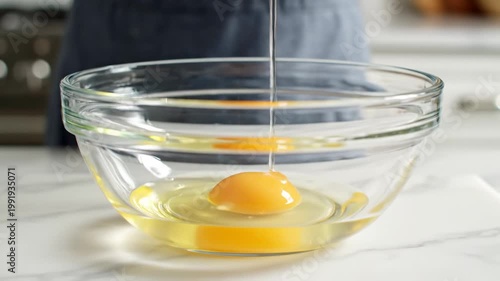 A close-up shot of a person cracking an egg into a clear glass bowl with a white napkin in the background.