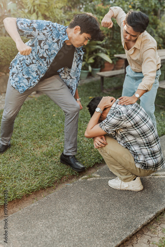 A frightened young Asian man shielding himself from two aggressive attackers during a violent confrontation in a tense outdoor setting. Outdoor shot.