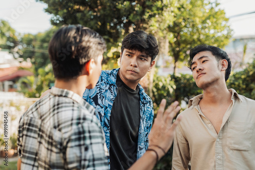 A anxious young Asian man trying to pacify two aggressive and hotheaded men during a tense argument. Outdoor shot.