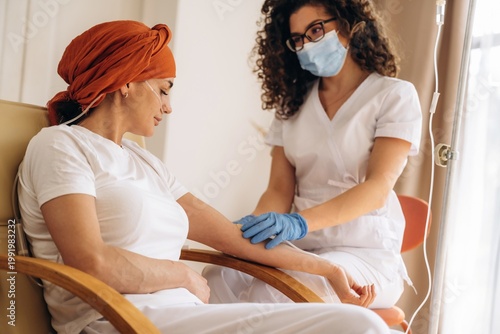 Vászonkép Female patient with headscarf receiving chemotherapy treatment from nurse in a h