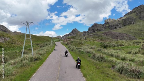 Two motorcyclists riding on a scenic winding road through green mountains.