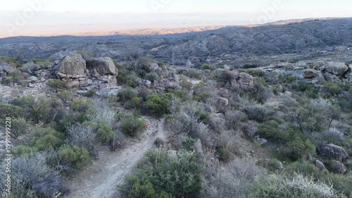 Hiking trail through rocky hills and shrubs in natural landscape at sunset