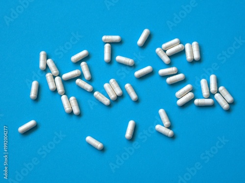 White capsules scattered on blue background, healthcare and pharmaceutical concept