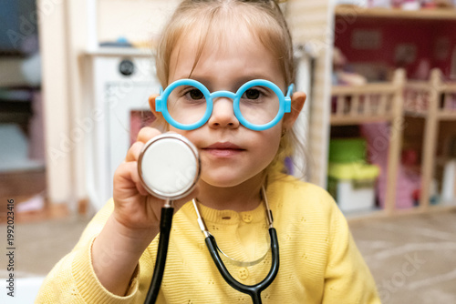 Toddler girl stethoscope closed mouth smile waist up dollhouse