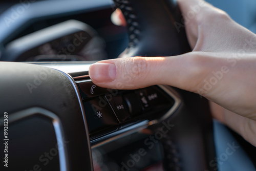 Tableau sur toile Close-up of finger pressing phone call button on steering wheel in modern car, with multimedia controls visible on multifunction panel