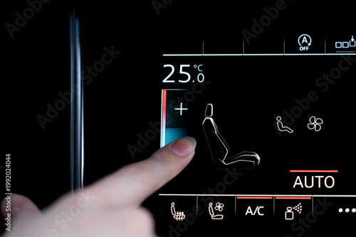 Finger touching touchscreen climate control to adjust front seat temperature setting in a modern car interior, close-up of digital automotive interface.