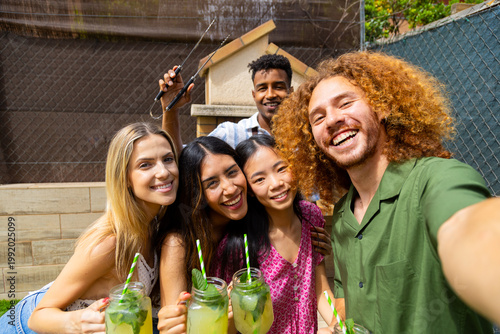 Happy friends taking selfie and drinking cocktails at barbecue party