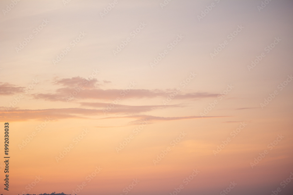 Obraz premium Warm golden sunset sky with soft, scattered clouds at twilight hour
