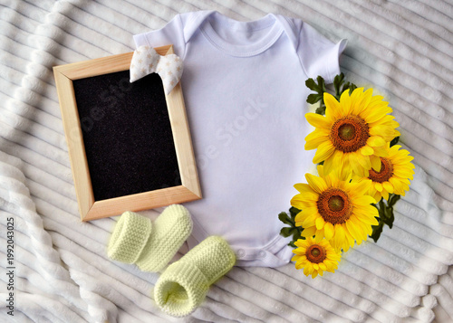 White baby bodysuit with blank chalkboard frame and sunflower decor. Seasonal announcement template for newborn birth or gender reveal. Cute baby clothes layout for social media background.