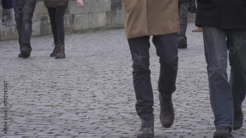  People's legs walking on cobblestone pavement in winter. Pedestrians in warm winter clothing and boots walk across a historic stone road. Close-up