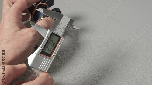 An engineer works with a digital caliper to measure a small robotic servo component with gears and wiring. Taking size, wide, length The precise measurement is shown on the LCD screen of the tool.