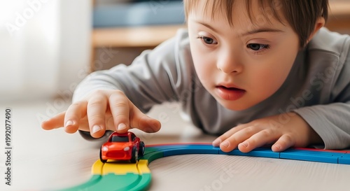 Child with Down syndrome playing with toy car on track. Happy boy focused on educational activity at home. Development game for kids cognitive learning, therapy and inclusion concept.