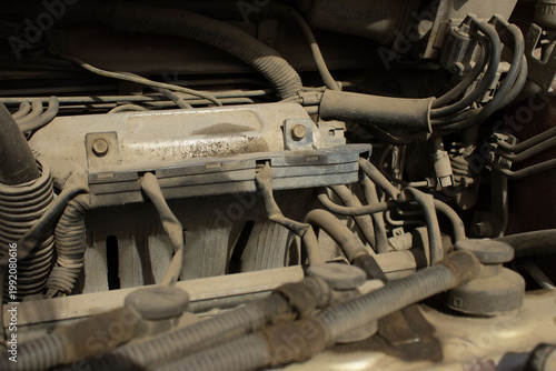 A detailed, macro-style photograph of a vehicle's engine bay, showing various dusty components including wires, hoses, and mechanical parts