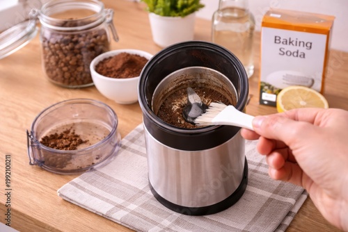 Cleaning Coffee Grinder with Brush and Baking Soda. Hand brushes coffee residue from an electric grinder, showing simple kitchen maintenance and natural deodorizing with baking soda.
