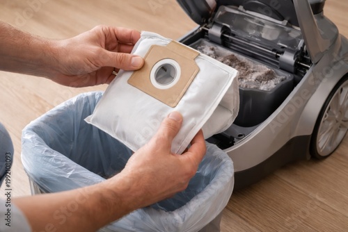 Replacing Vacuum Cleaner Bag During Home Cleaning. Hands remove a full vacuum dust bag above a trash bin, showing simple appliance maintenance and hygienic home cleaning.