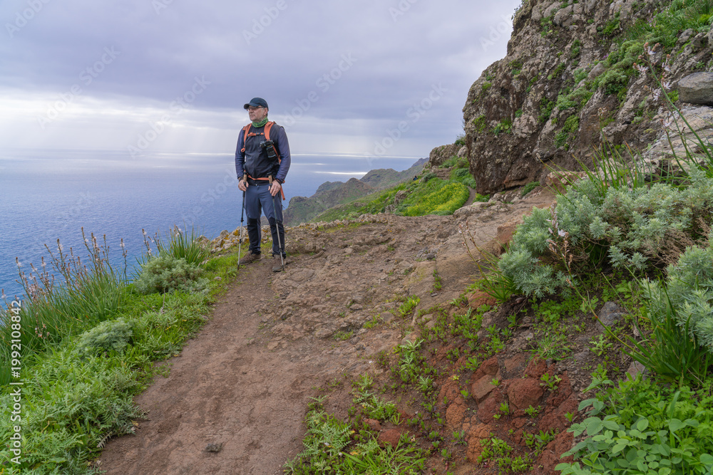 Obraz premium A hiker stands on a nature trail in Anaga Rural Park, with the ocean in the background. Tenerife. Canary Islands.