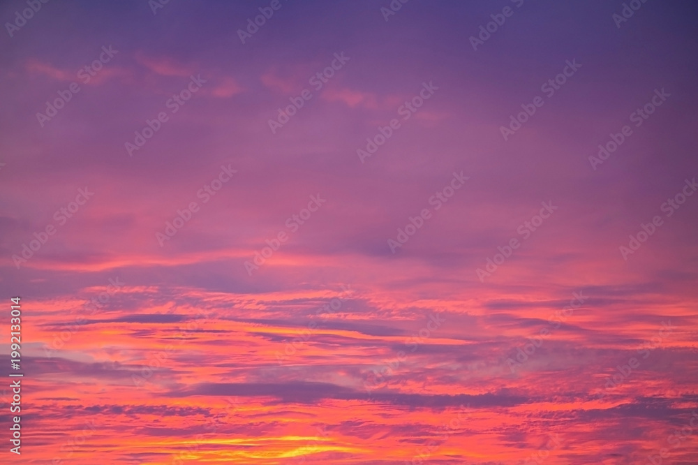 Obraz premium Vibrant layers of purple, pink and orange clouds fill the sky in a stunning sunset scene