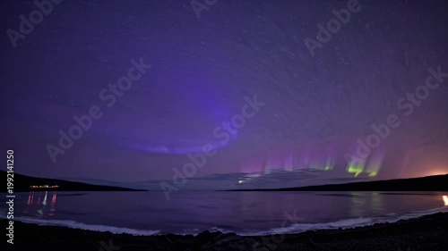 Northern Lights display over calm water, vibrant green and purple auroras swirling in the night sky, with distant lights reflecting on the serene surface of the lake