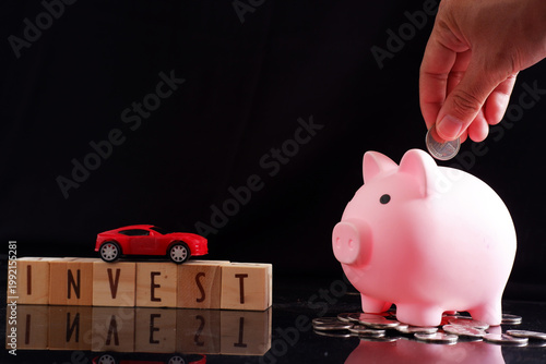 Putting coins in a piggy bank, miniature cars on the office desk, planning and calculating to save, visualizing planning to buy a new car, dream visualization, financing
