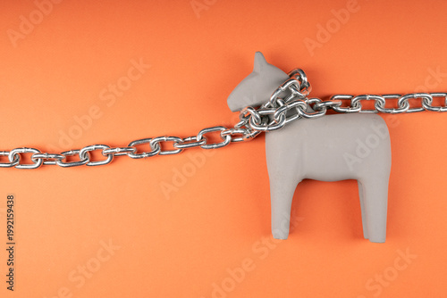 Miniature wooden horse chained on orange background, captivity and restraint symbolism