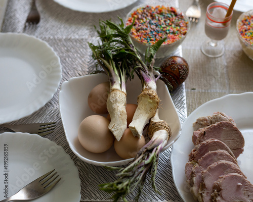 Horseradish and eggs on a plate. Next to them are plates, forks, and a plate of meat.