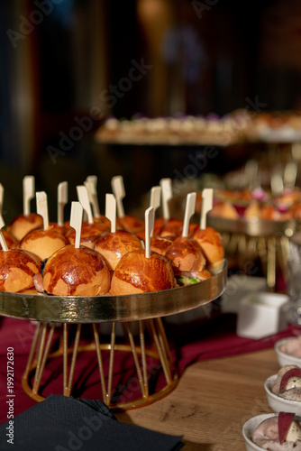 Close-up of gourmet mini sliders on an elegant stand, served at a stylish buffet with warm lighting and a festive, upscale party atmosphere.