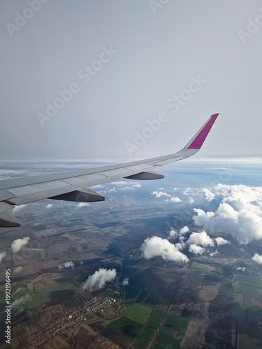 Breathtaking landing with a plane wing banking through thick, foggy clouds. View through airplane window during flight, with dynamic aerial perspective of the earth