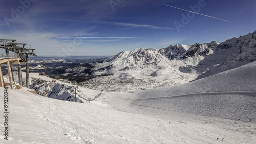 Snowy mountain landscape with ski slopes and chairlift in the distance during the day in winter. Kasprowy Wierch, Zakopane, Poland