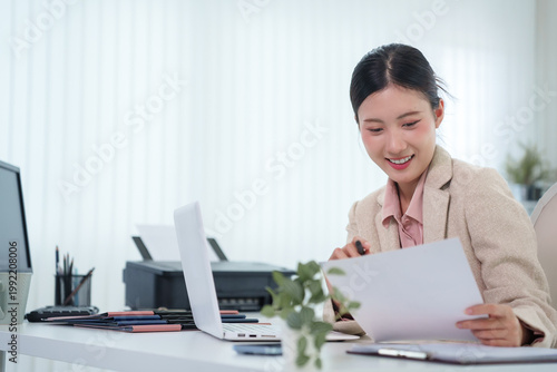 Tableau sur toile Asian businesswoman reviewing document paper report smiling at modern office des